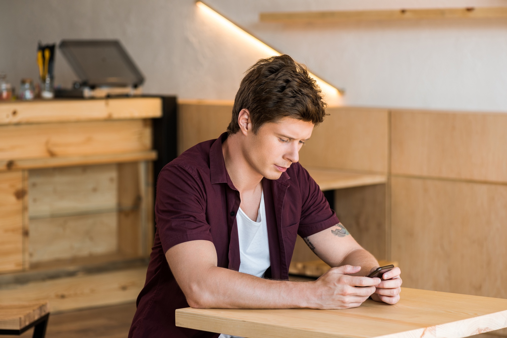 handsome young man using smartphone while sitting at table in cafe