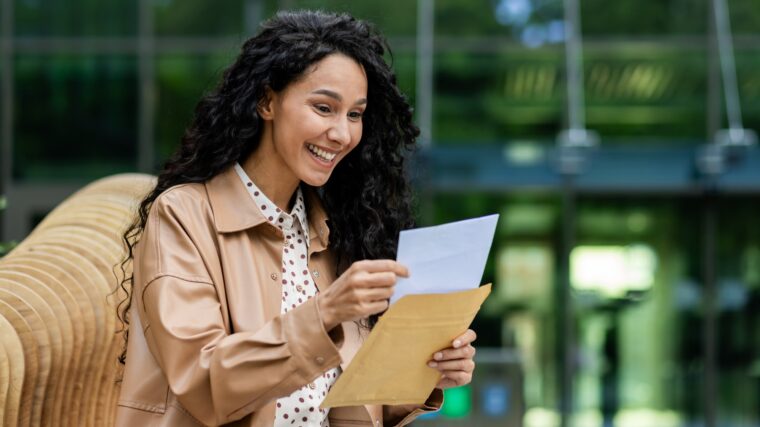 Woman reading a letter outdoor, relaxed setting with nature backdrop